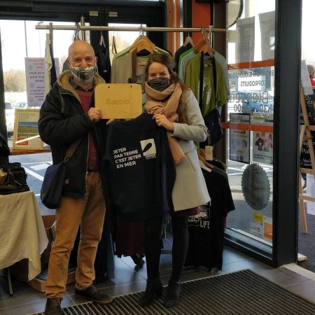 photo de loic de saobio avec une membre de surfrider calvados pour le don des sweats à capuches imprimés avec le logo surfrider